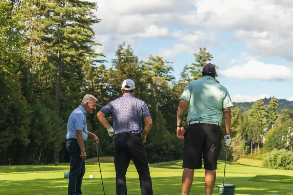 Three golfers engaging in strategy discussion on a lush golf course with a scenic backdrop of trees.