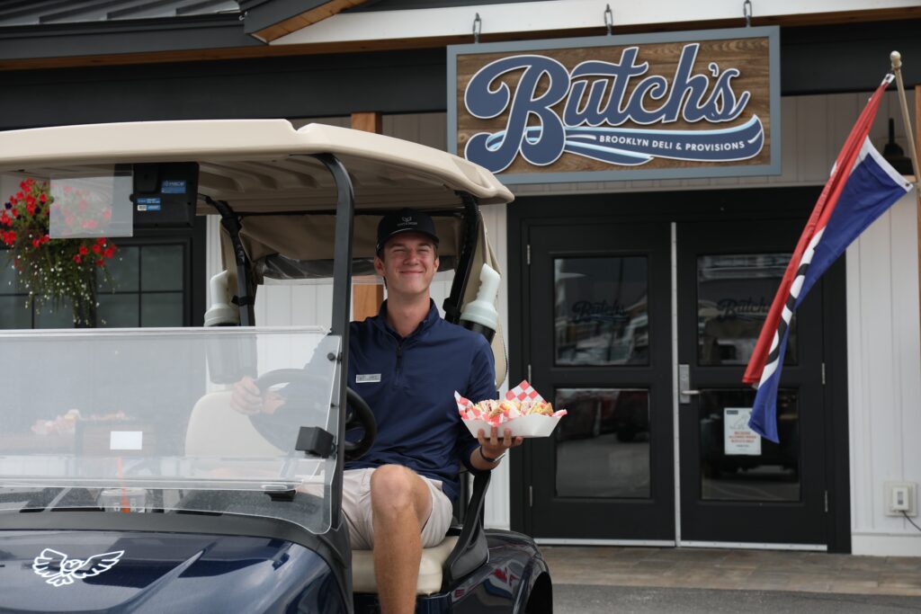 Guest holding food outside Butch’s Brooklyn Deli at Owl’s Nest Resort with golf cart