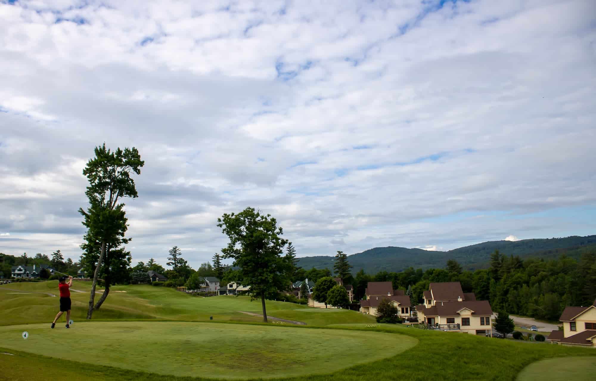 Golfer teeing off during the NHGA Four-Ball Tournament at Owl’s Nest Resort with scenic White Mountains views in New Hampshire.